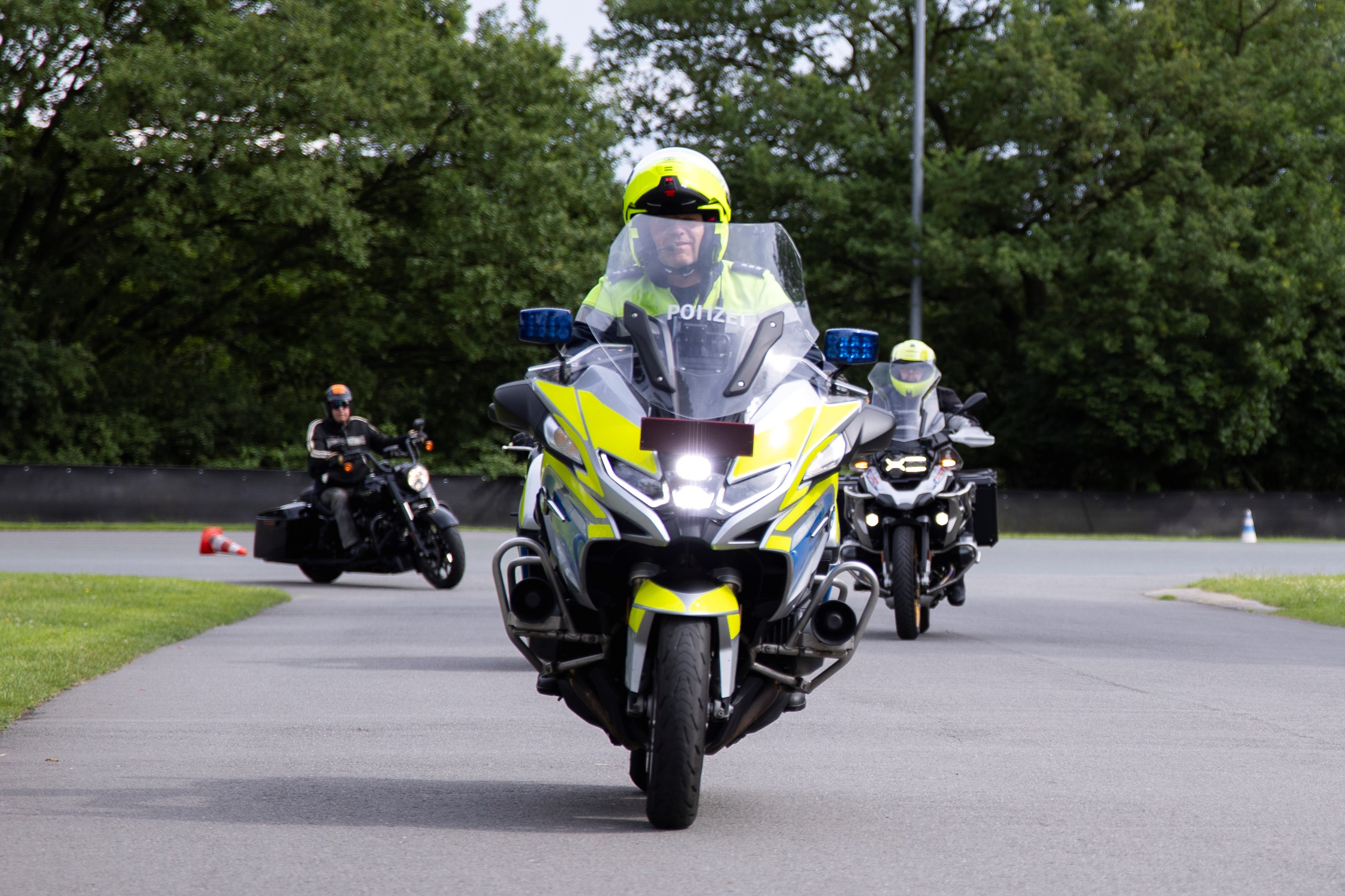 Polizist auf einem Polizeimotorrad. Zwei weitere Kräder im Hintergrund.
