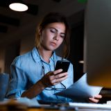 Eine junge Frau an ihrem Arbeitsplatz schaut auf ihr Smartphone
