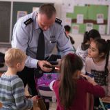 Polizeihauptkommissar Holger Siegburg erklärt Grundschülern, wie ein Blinklicht-Anhänger an einem Tornister funktioniert.
