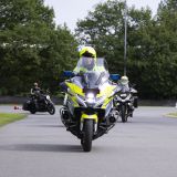 Ein Polizeibeamter auf einem Polizeimotorrad und Teilnehmende der PoliTour 2024 drehen eine Runde auf dem ADAC-Übungsgelände in Haltern am See.