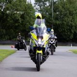 Polizist auf einem Polizeimotorrad. Zwei weitere Kräder im Hintergrund.