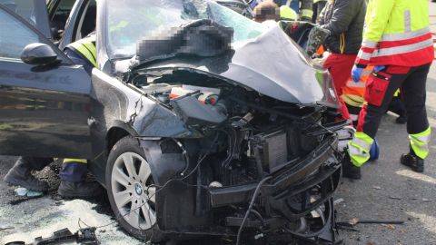 Total beschädigtes Unfallfahrzeug; Rettungskräfte arbeiten an dem Pkw.