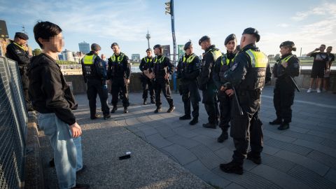 Police officers surround a 14-year-old boy before taking him to the police station. The Rhine can be seen in the background.