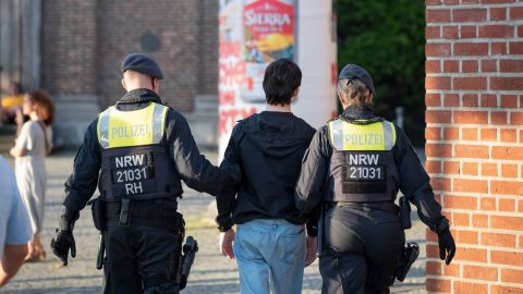 A 14-year-old boy is taken away by a policeman and a policewoman in Düsseldorf's old town. A church can be seen in the background.