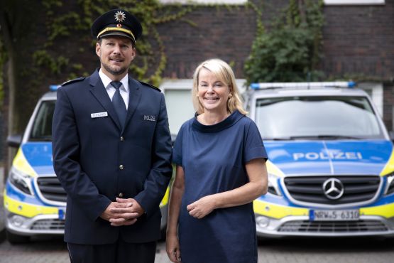 Daniel Sühling und Polizeipräsidentin Friederike Zurhausen stehen vor zwei Streifenwagen der Polizei